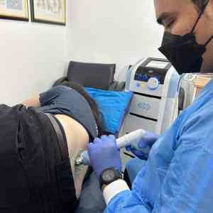 Physiotherapist using shockwave therapy for a female patient during back pain treatment in KL